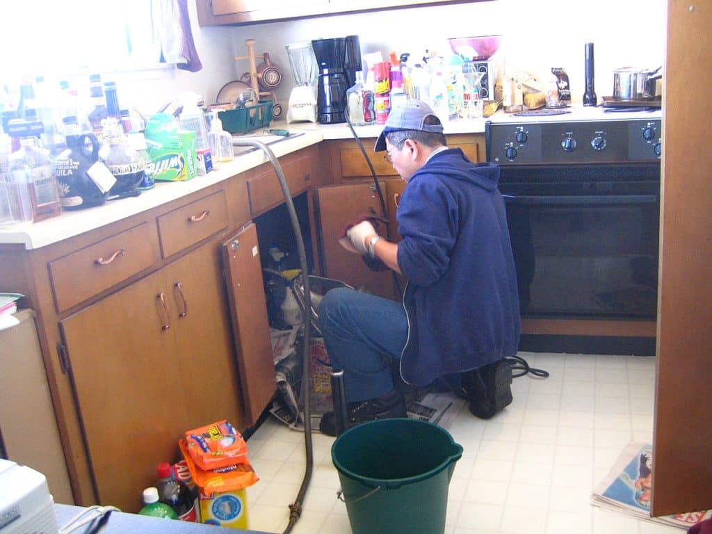 Plumber fixing a pipe in a kitchen, Plumber Advertising Agency.