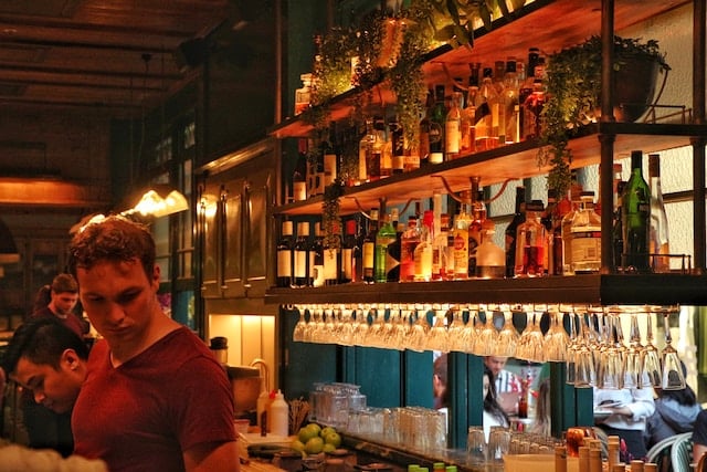 A bartender with wine bottles (behind), Wine Advertising Agency.
