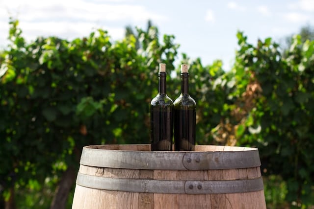 Wine bottle on a barrel with grapes field in background, Wine Advertising Agency.