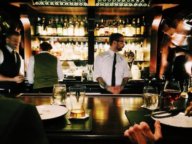 Bartenders serving the customer with liquor bottles (behind), Liquor Store Advertising.